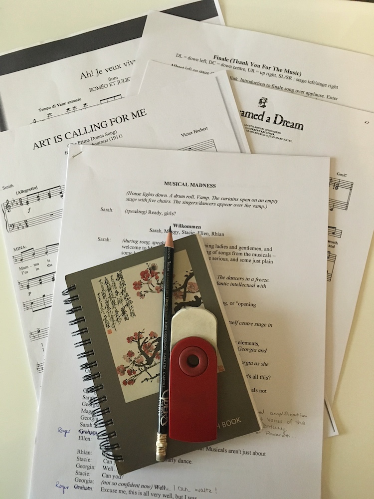 A pile of loose rehearsal sheet music, a small notebook, a pencil, an eraser