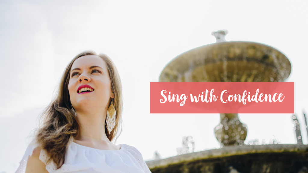 Georgia, a white woman in her 20s with blonde hair, blue eyes and pink lipstick is smiling while looking off to the upper right corner of the frame. She is wearing beaded fringe earrings and a white top. Behind her is a golden fountain and overlain on the fountain is a pink text box with white cursive writing inside that says 'Sing With Confidence' - she is looking forward to telling you how you can work on building singing confidence yourself. 