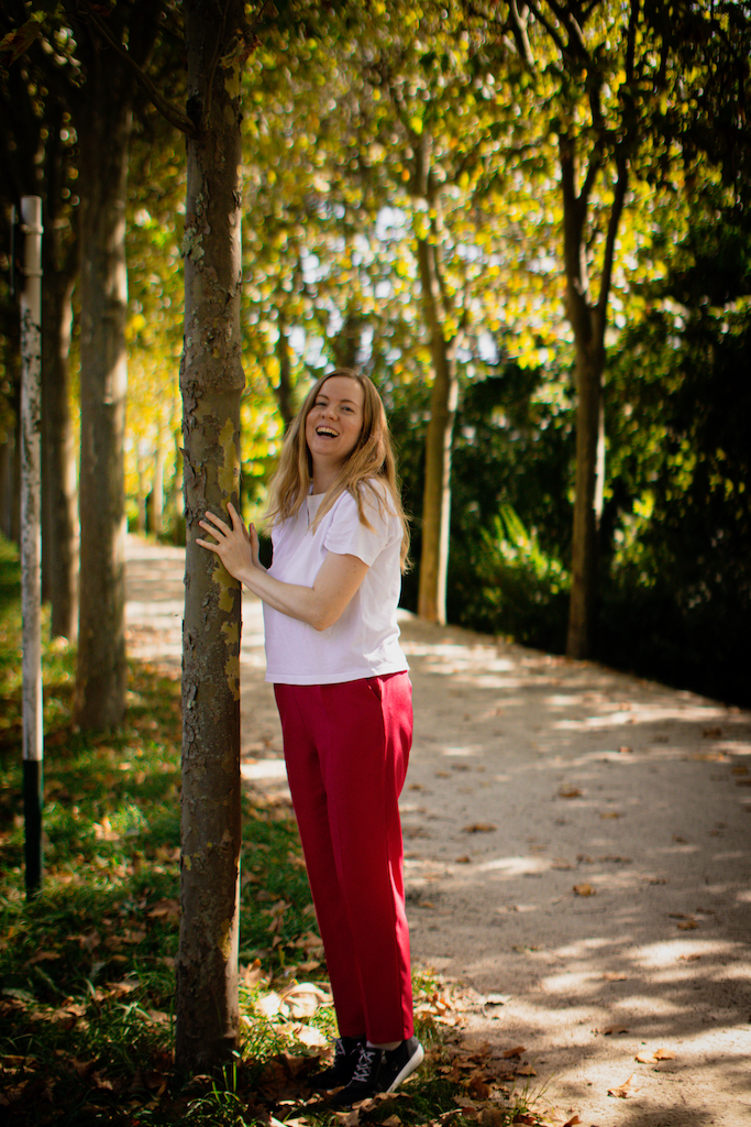 Georgia is standing on a tree-lined path, leaning against a tree and laughing at the camera