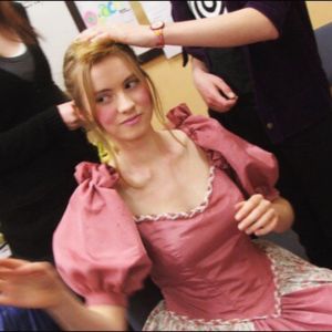 Georgia Aussenac is 16 years old, sitting down in a blush pink costume gown, with hands around her doing her hair.