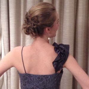 Georgia Aussenac is standing back to the camera, hands on hips, head turned to one side, showing off her glamorous updo, asymmetrical silver sequin gown with a frill strap, and pearl drop earrings.